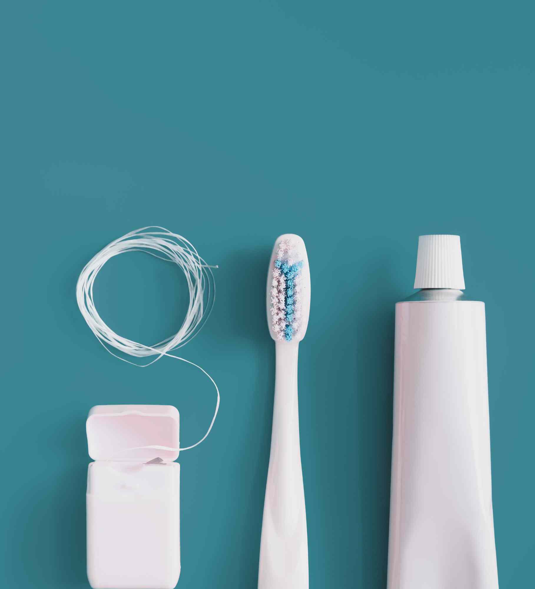 Dental floss, a toothbrush and a tube of toothpaste laid out on a teal background